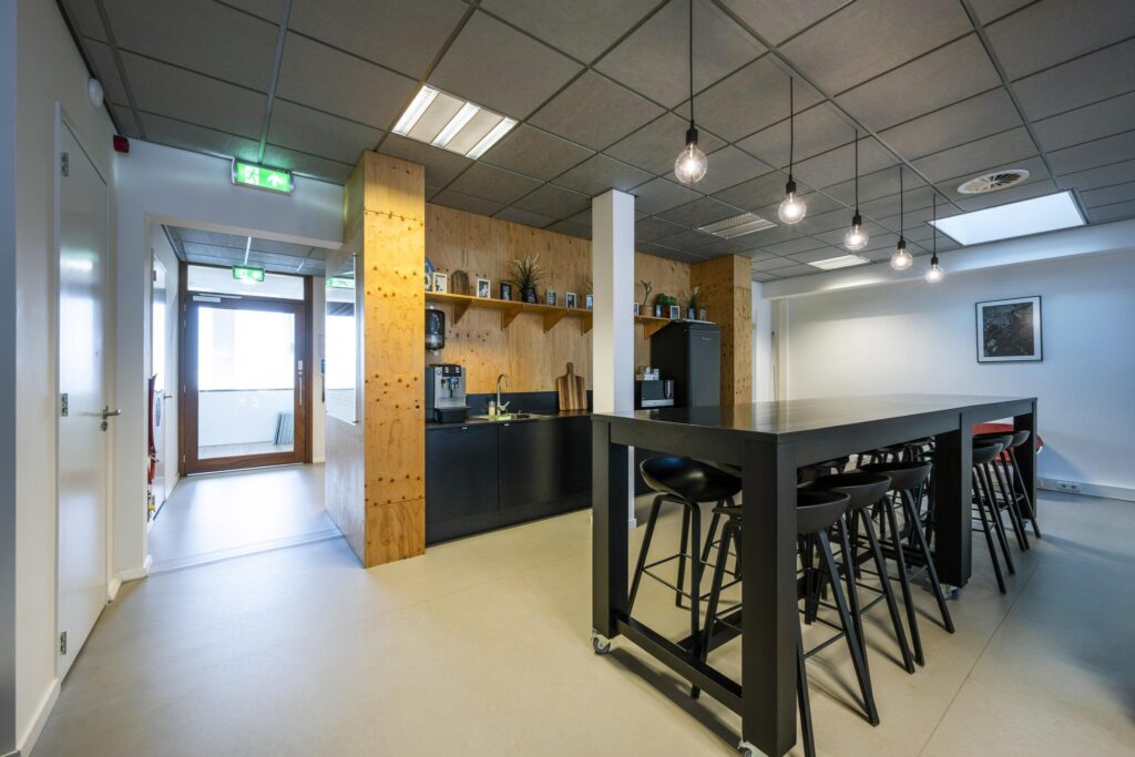 Moderne kantoorkeuken aan de De Ruijterkade met een lange zwarte tafel, barkrukken en koffiecorner.